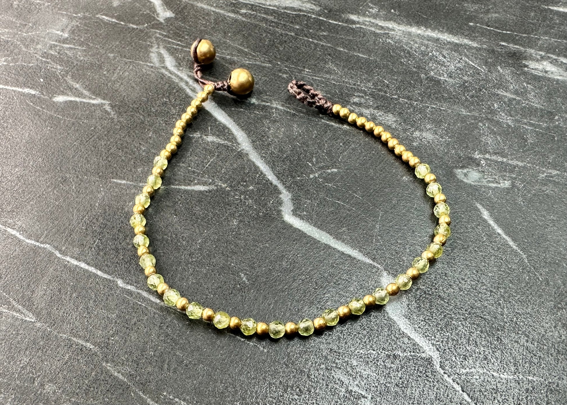 A crystal healing bracelet made of faceted Peridot crystals on a cotton cord with brass beads