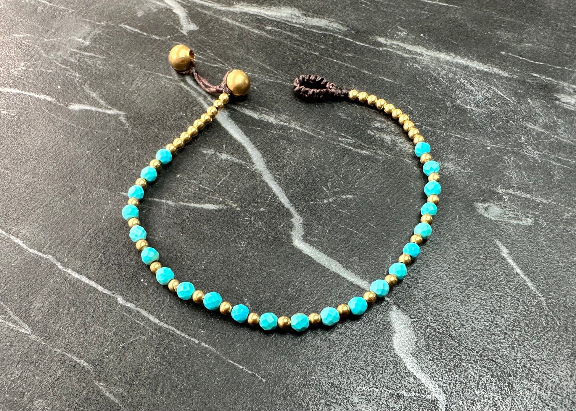 A crystal healing bracelet made of faceted Turquoise crystals on a cotton cord with brass beads.