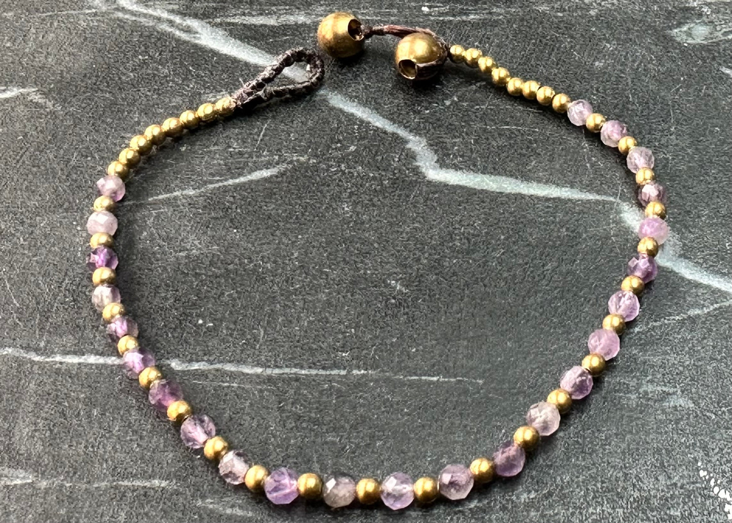 A crystal healing bracelet made of faceted Amethyst crystals on a cotton cord with brass beads.