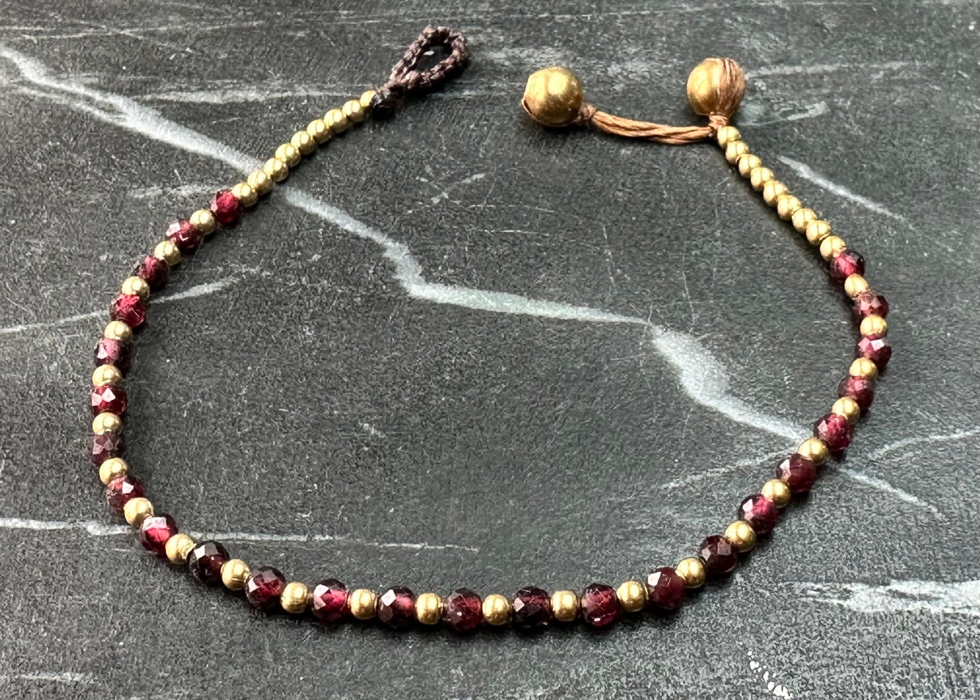 A crystal healing bracelet made of faceted Ruby crystals on a cotton cord with brass beads.