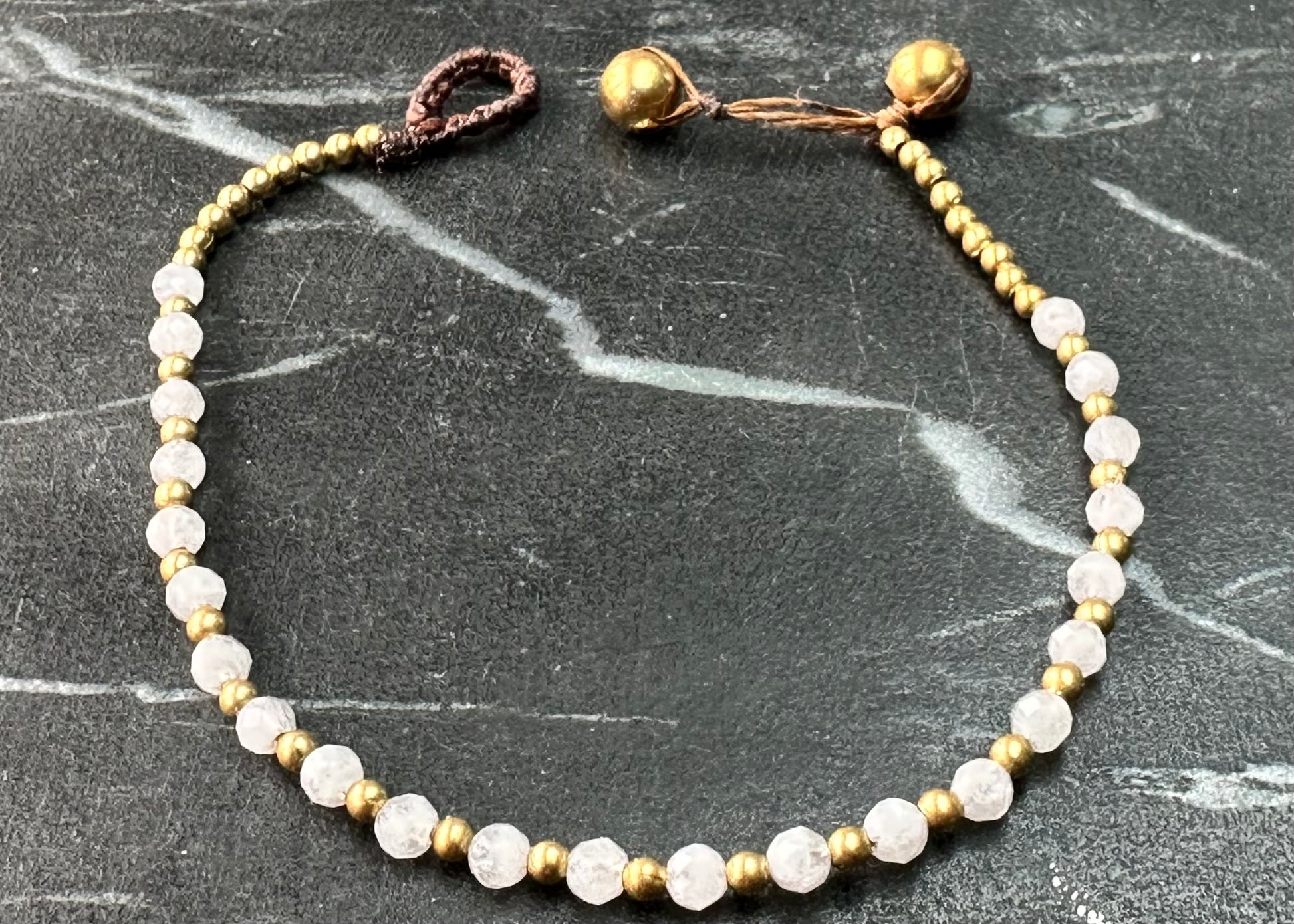 A crystal healing bracelet made of faceted Moonstone crystals on a cotton cord with brass beads.