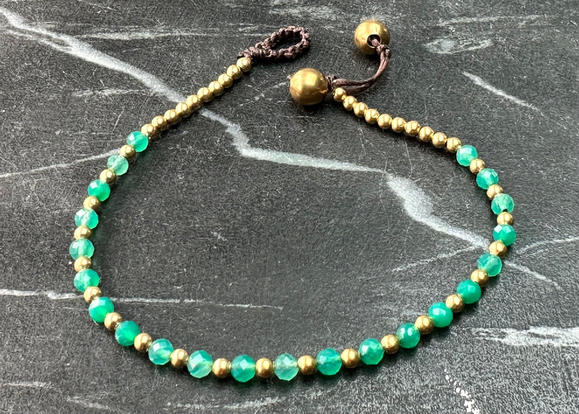 A crystal healing bracelet made of faceted Aventurine crystals on a cotton cord with brass beads.