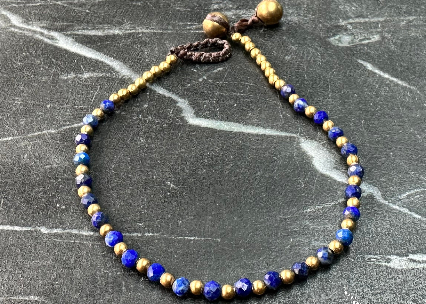 A crystal healing bracelet made of faceted Lapis crystals on a cotton cord with brass beads.