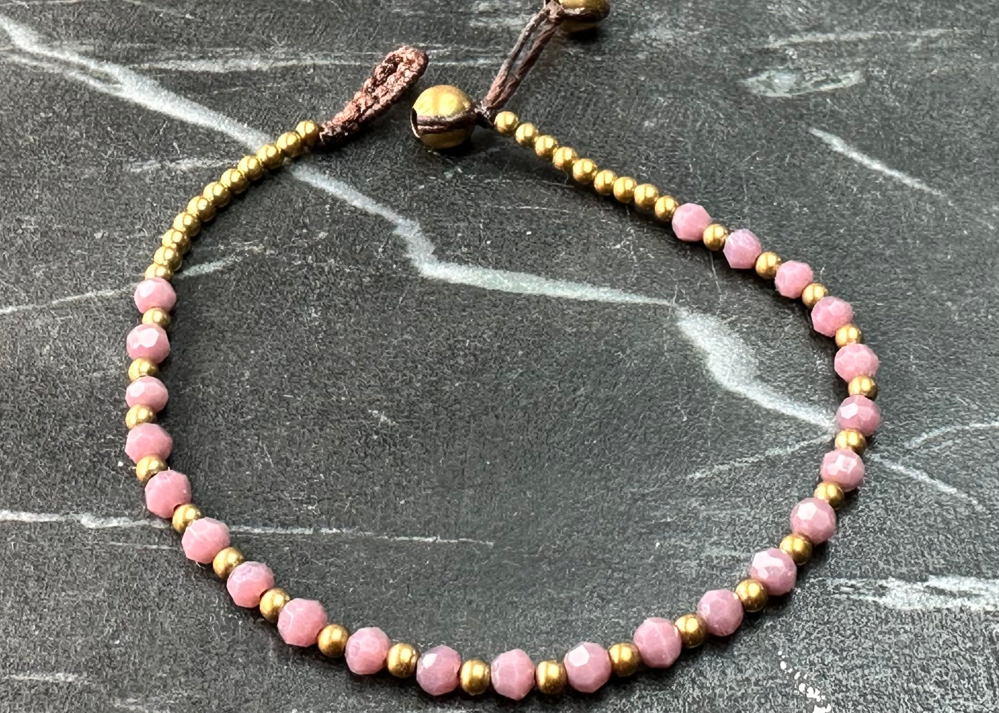 A crystal healing bracelet made of faceted Pink Tourmaline crystals on a cotton cord with brass beads.