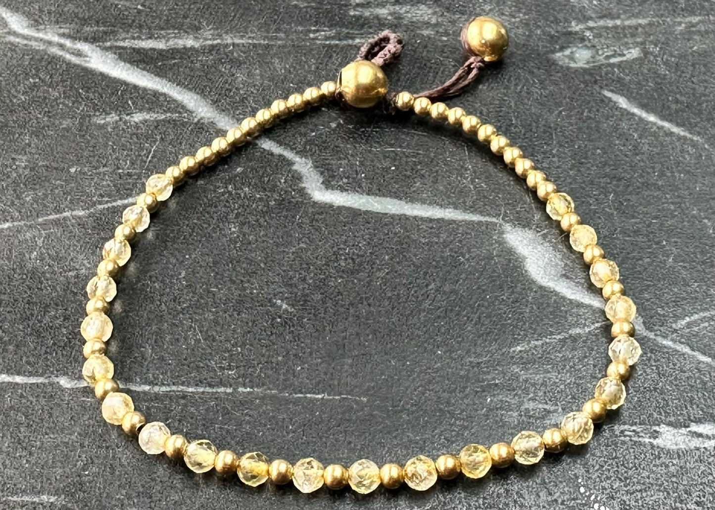 A crystal healing bracelet made of faceted Citrine crystals on a cotton cord with brass beads.