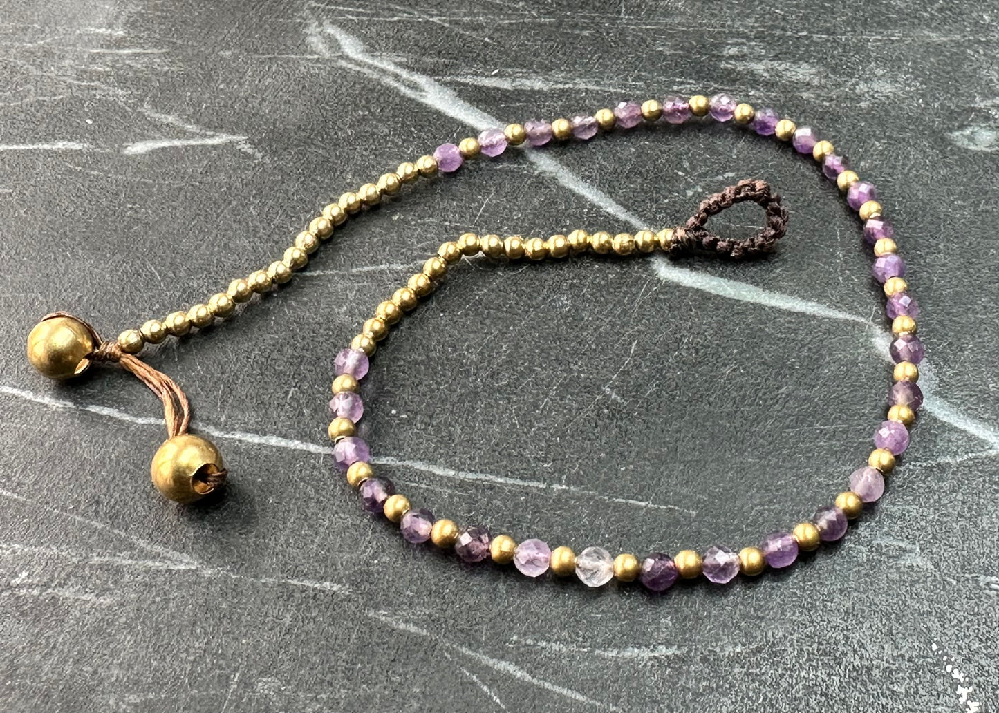 A crystal healing bracelet made of faceted Amethyst crystals on a cotton cord with brass beads