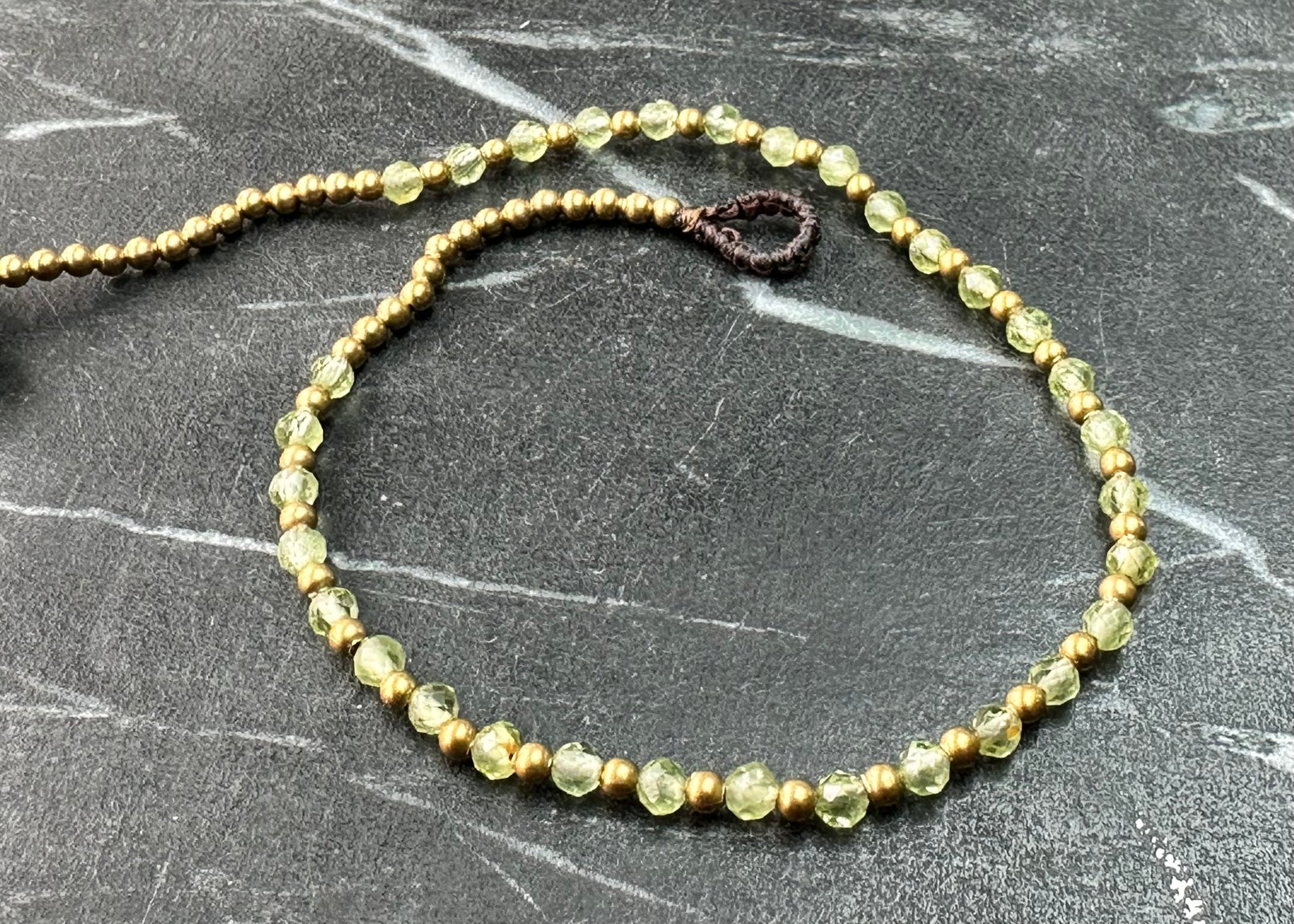 A crystal healing anklet made of faceted Peridot crystals on a cotton cord with brass beads