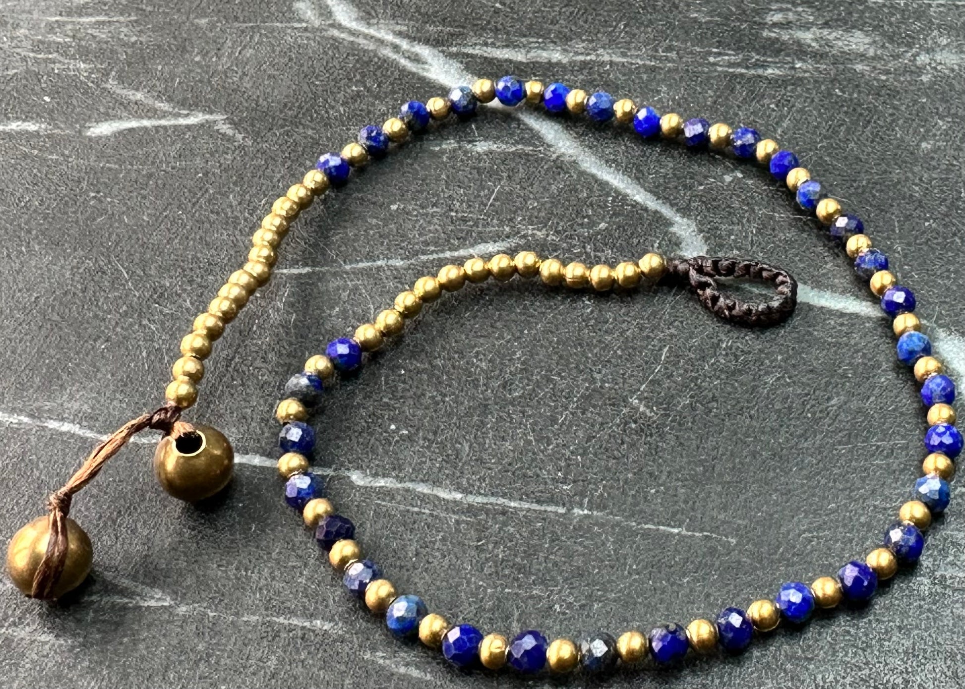 A crystal healing anklet made of faceted Lapis crystals on a cotton cord with brass beads