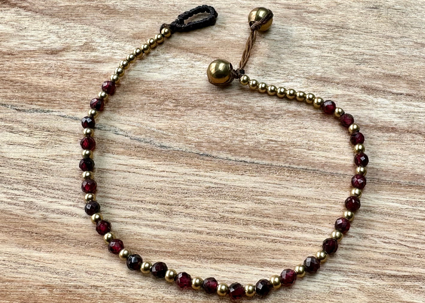 A crystal healing bracelet made of faceted Garnet crystals on a cotton cord with brass beads.