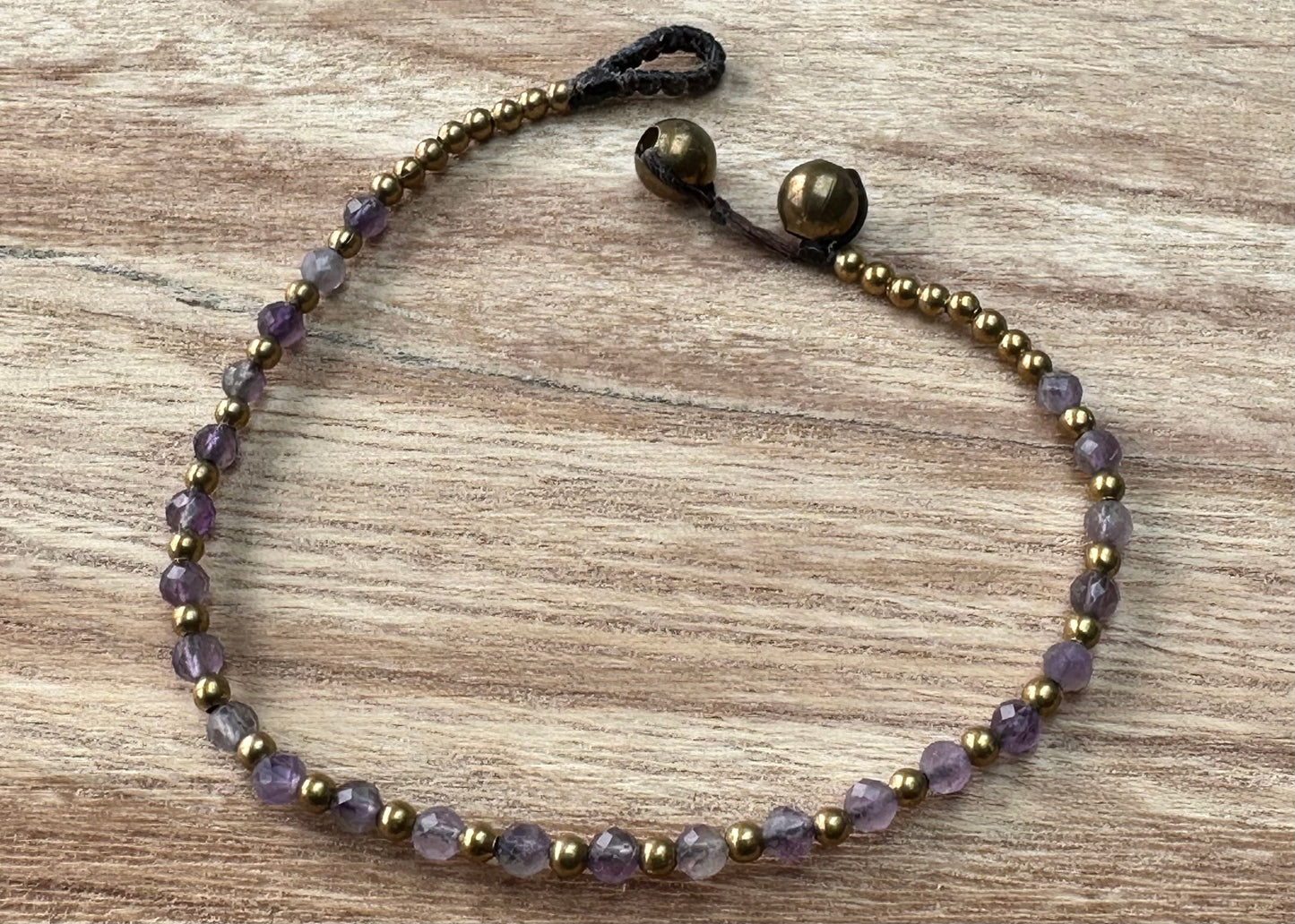 A crystal healing bracelet made of faceted Amethyst crystals on a cotton cord with brass beads.