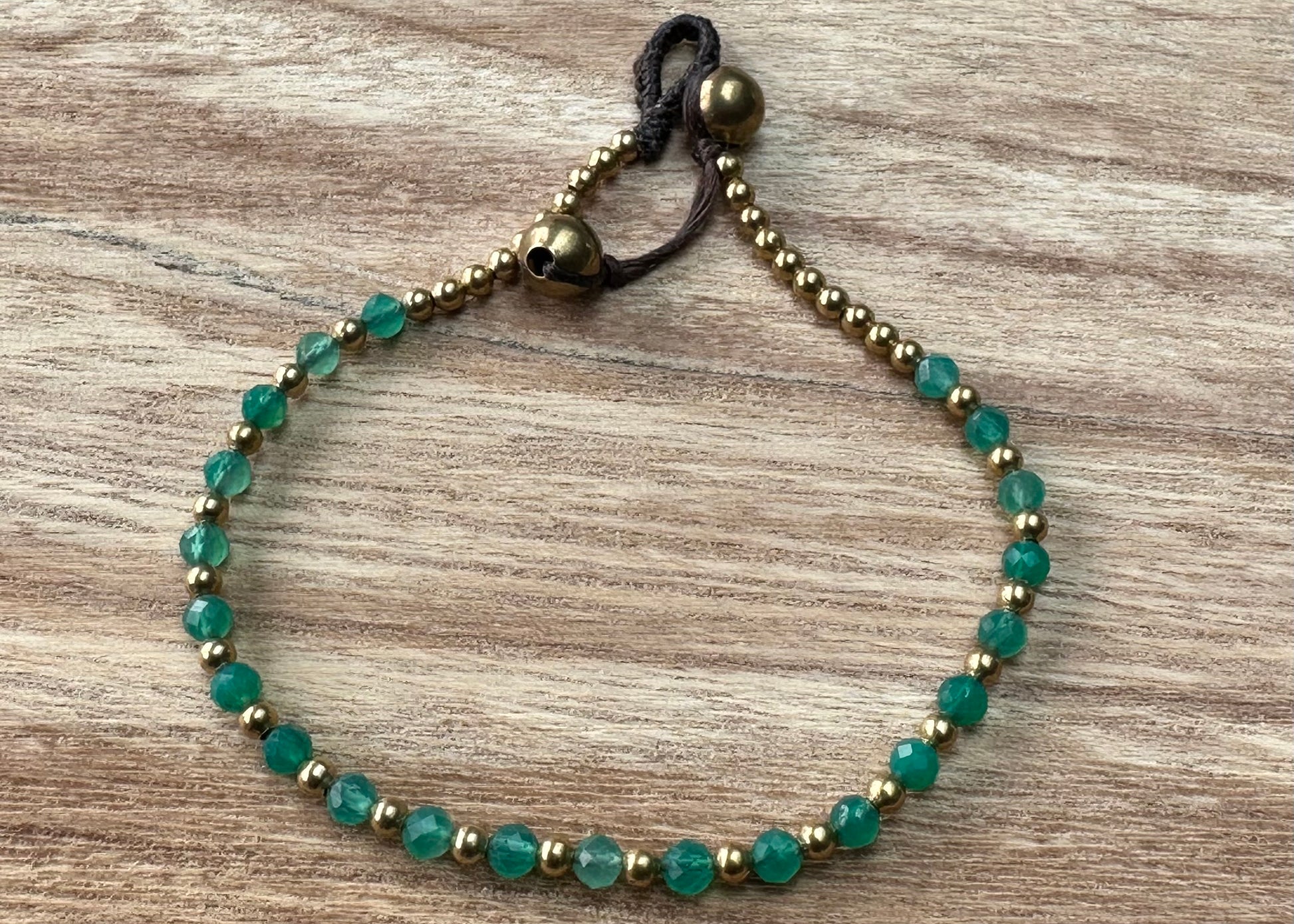 A crystal healing bracelet made of faceted Aventurine crystals on a cotton cord with brass beads.