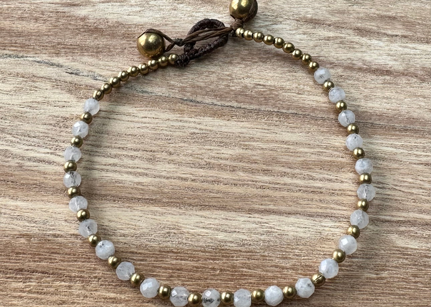 A crystal healing bracelet made of faceted Moonstone crystals on a cotton cord with brass beads.