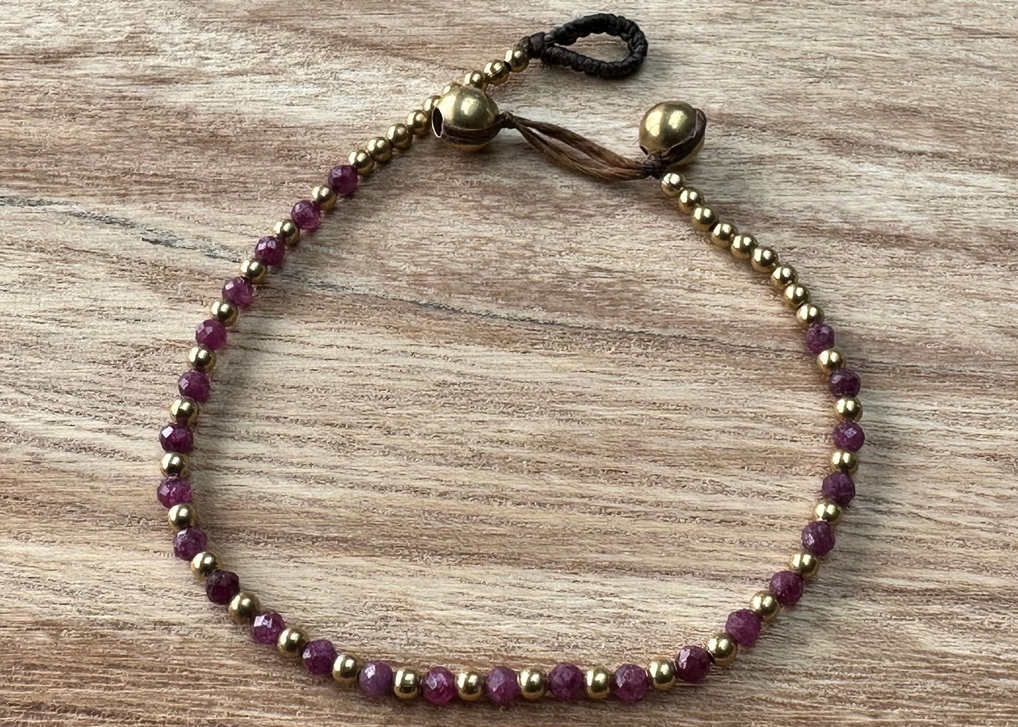 A crystal healing bracelet made of faceted Ruby crystals on a cotton cord with brass beads.