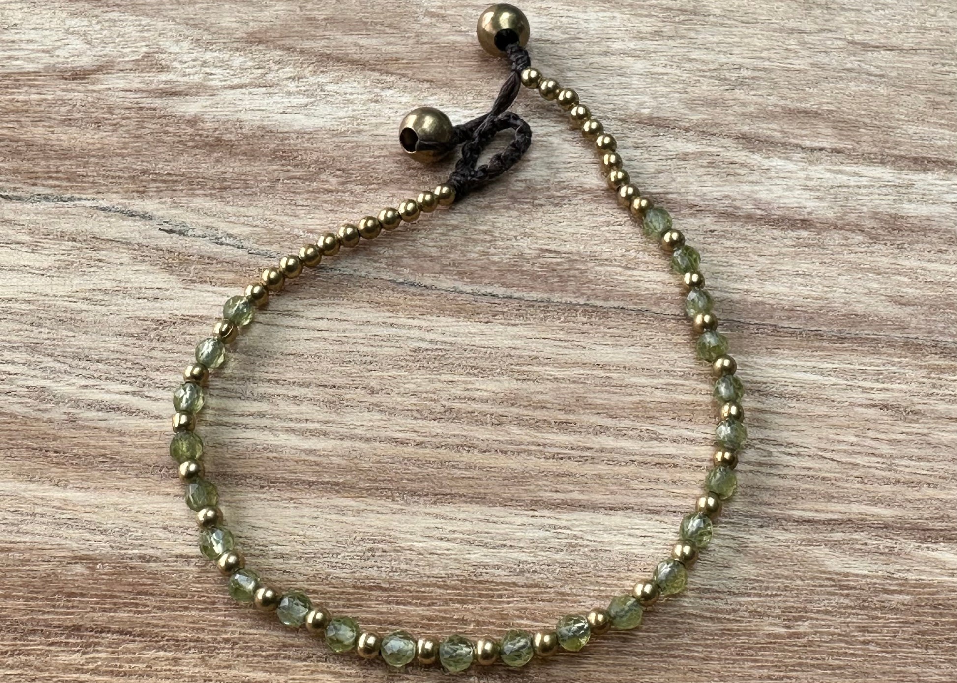 A crystal healing bracelet made of faceted Peridot crystals on a cotton cord with brass beads.