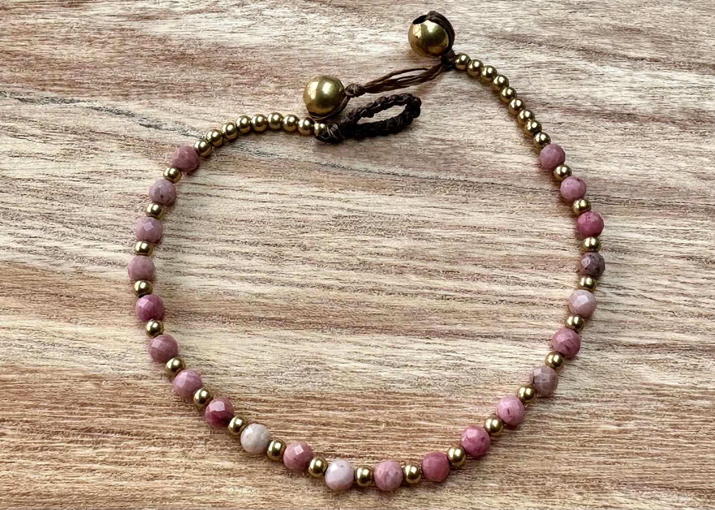 A crystal healing bracelet made of faceted Pink Tourmaline crystals on a cotton cord with brass beads.