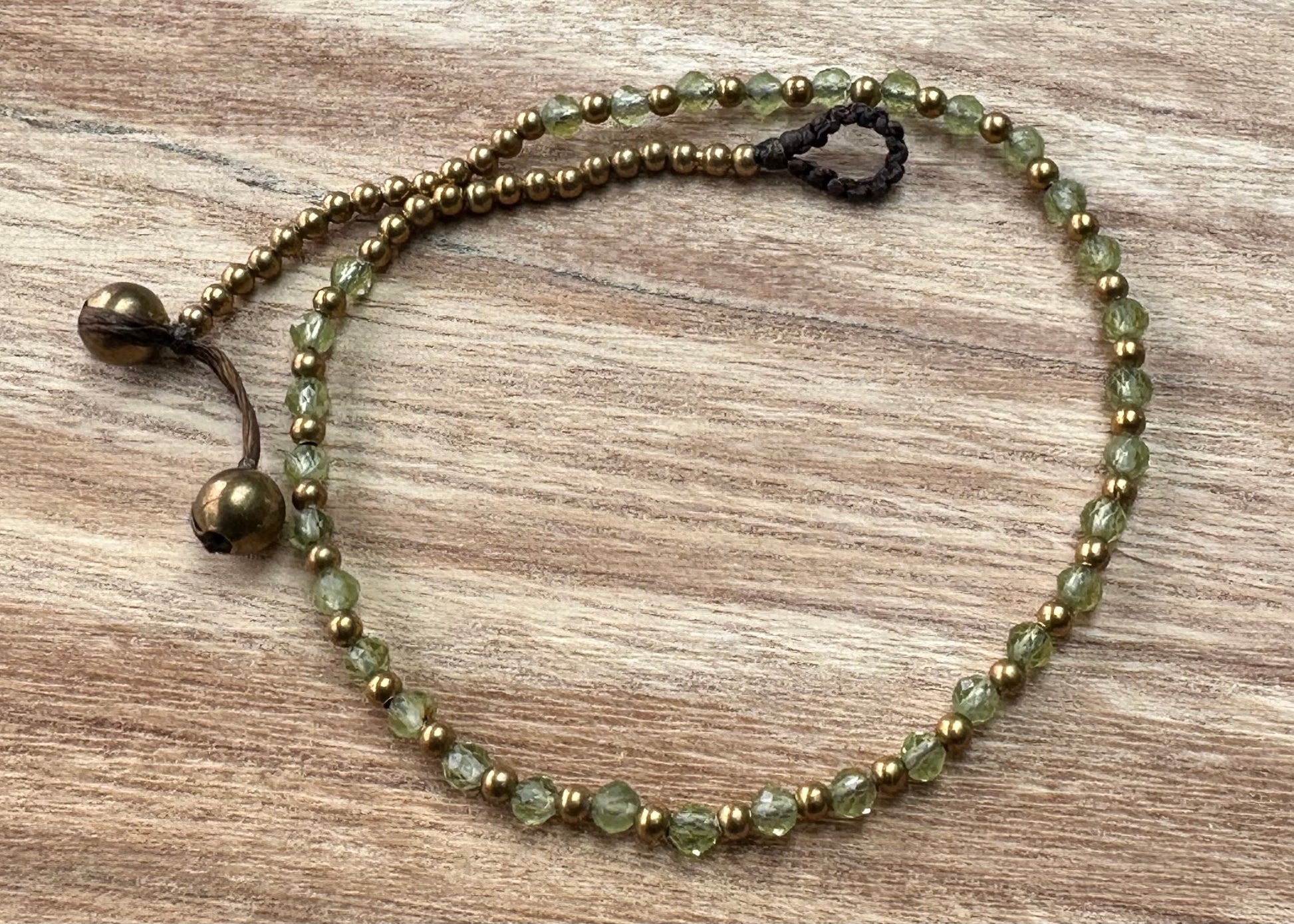 A crystal healing anklet made of faceted Peridot crystals on a cotton cord with brass beads