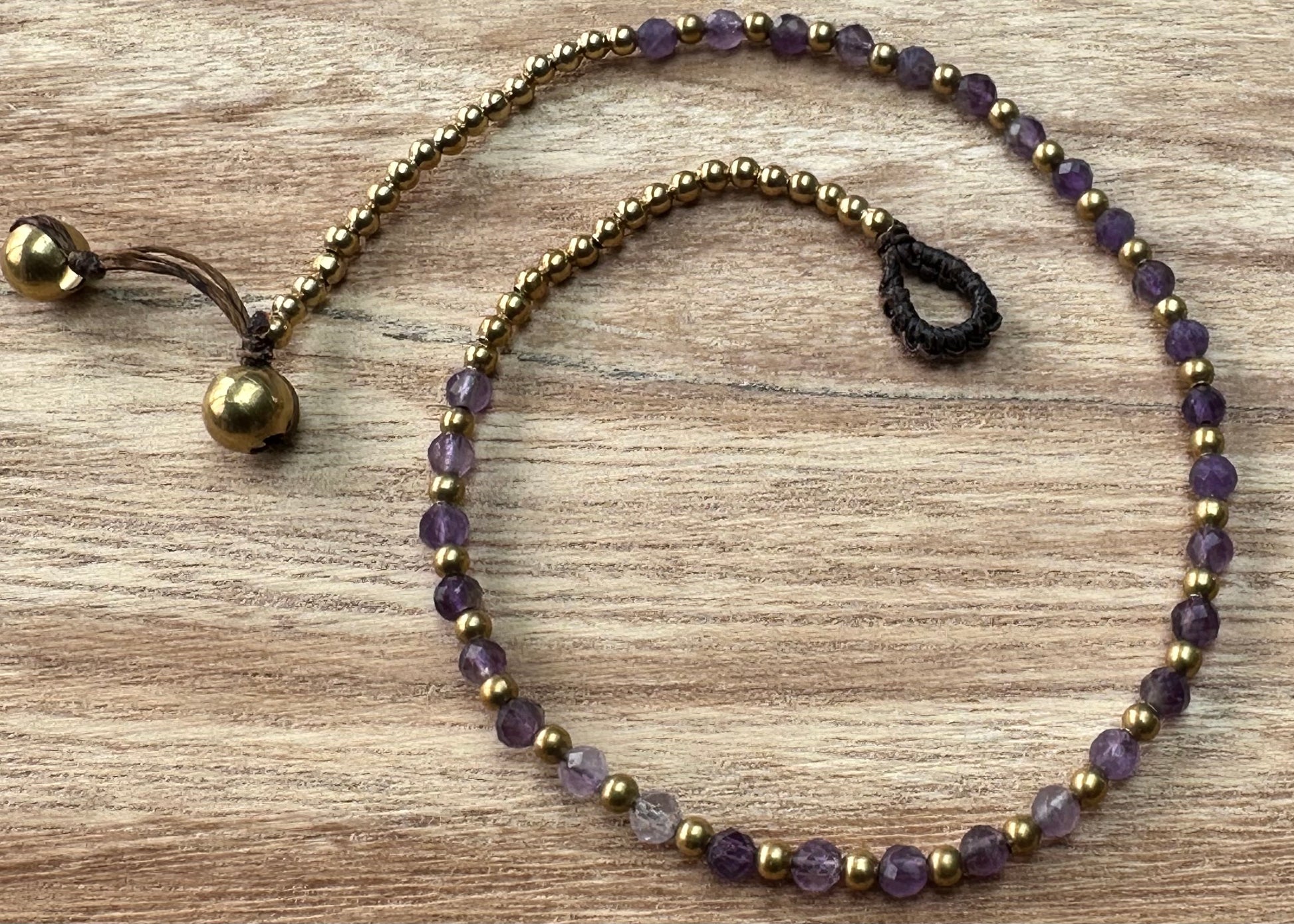 A crystal healing anklet made of faceted Amethyst crystals on a cotton cord with brass beads