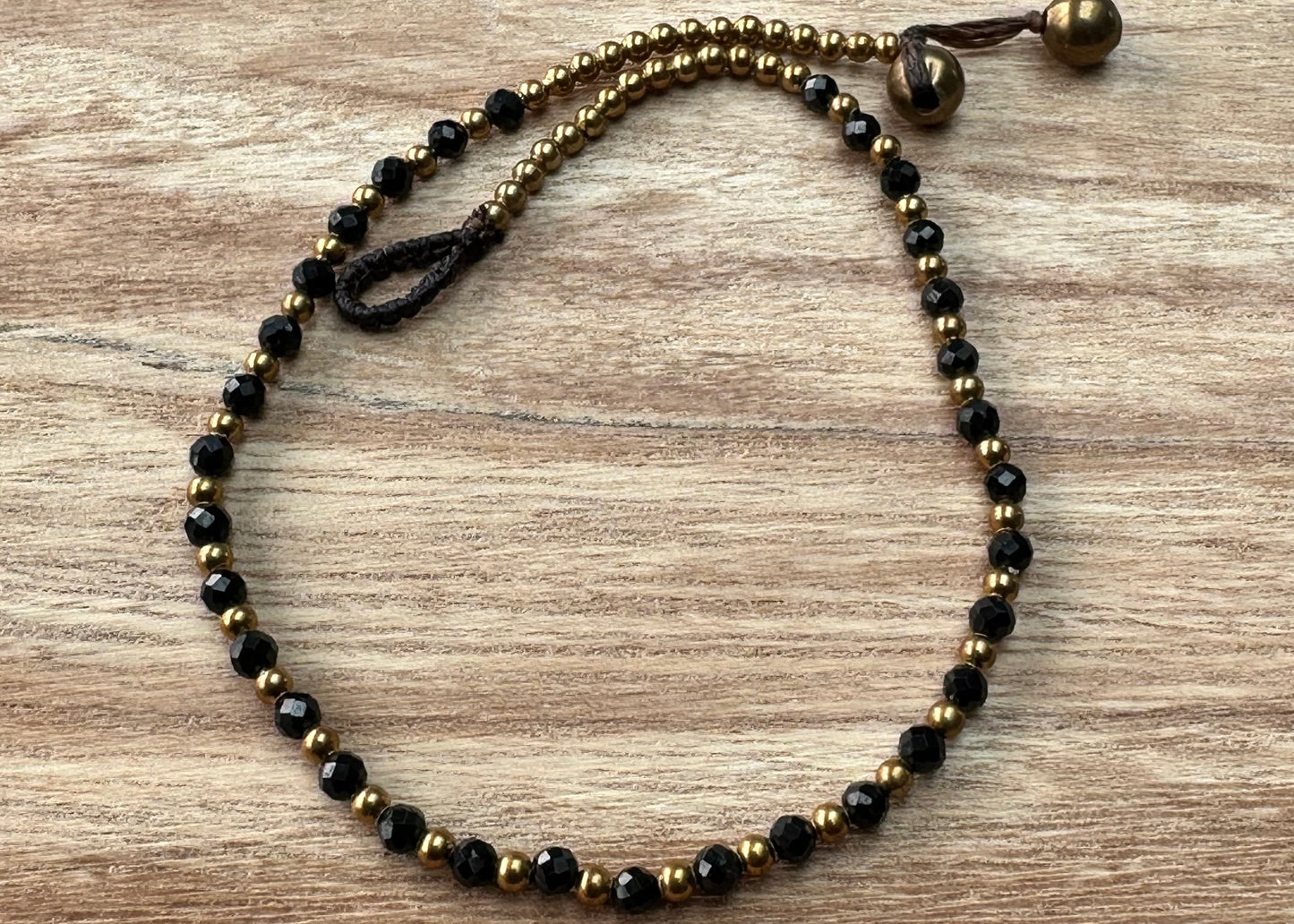 A crystal healing anklet made of faceted Black Spinel crystals on a cotton cord with brass beads.